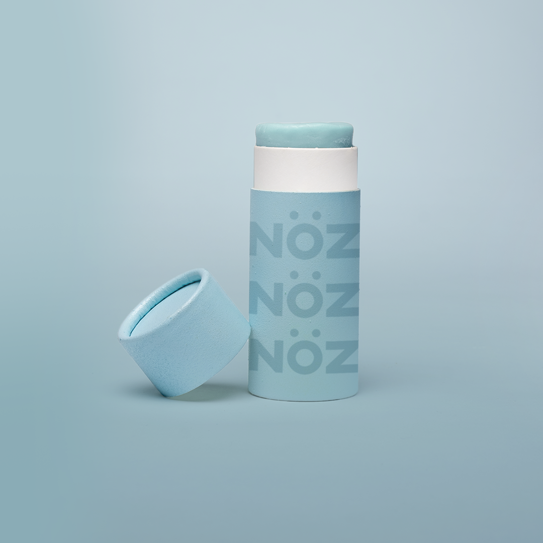 Blue Noz stick sunscreen with the cap off modeled in a Blue background