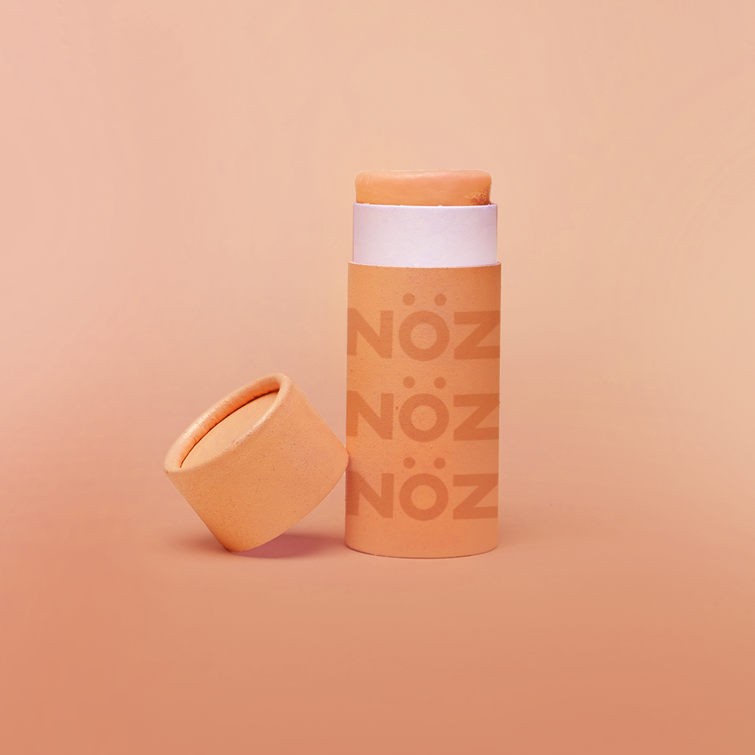 Orange Noz stick sunscreen with the cap off modeled in an Orange background