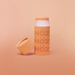 Load image into Gallery viewer, Orange Noz stick sunscreen with the cap off modeled in an Orange background
